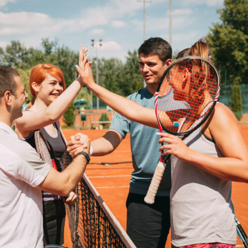 Four young friends giving a high-five after tennis training. Selective focus.