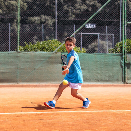 Little boy in sportswear playing tennis on a dirt tennis court striving to do his best