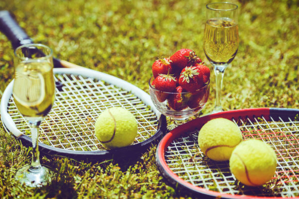 Tennis game. Strawberries, champagne and tennis balls with rackets on the green grass. Sport, recreation concept