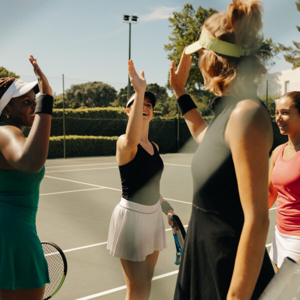 Group of women celebrating on a tennis court, waving and high-fiving each other after a successful team match. Happy and supportive sports environment.