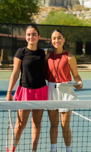 Cheerful caucasian teen girl and latin woman coach on the tennis court smiling while at tennis school